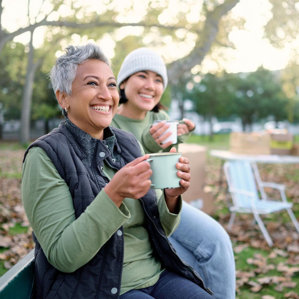 Older Woman Sitting on Park Bench with Young Woman While Drinking Hot Beverages