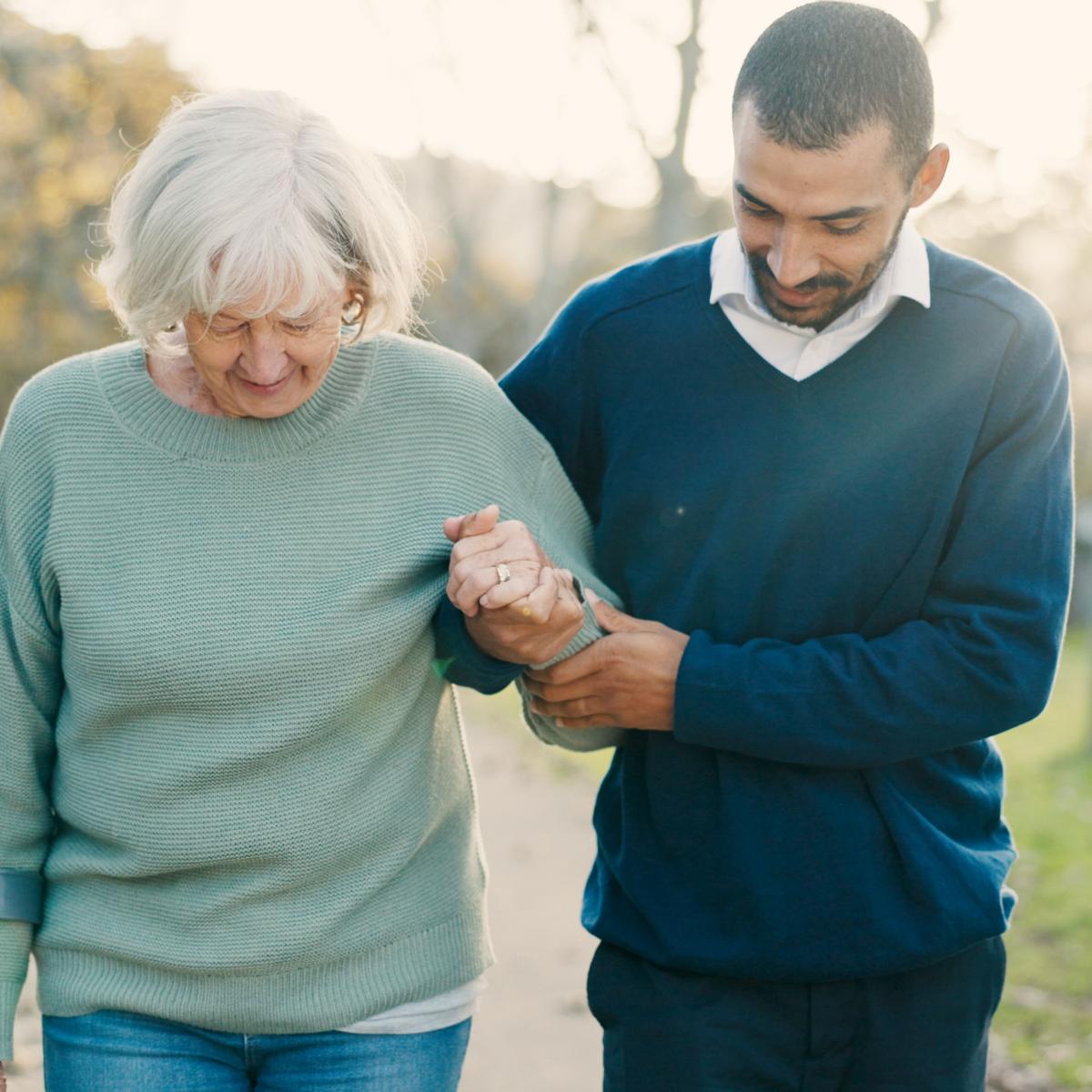 Older Woman Receives Help Walking by Younger Man Outside