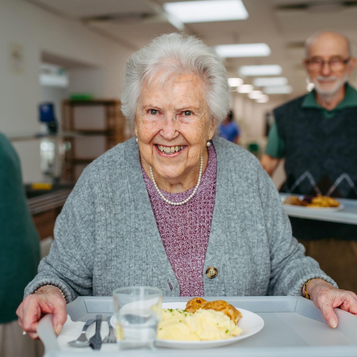 Older Adult Woman Smiles While Holding a Food Tray in a Cafeteria