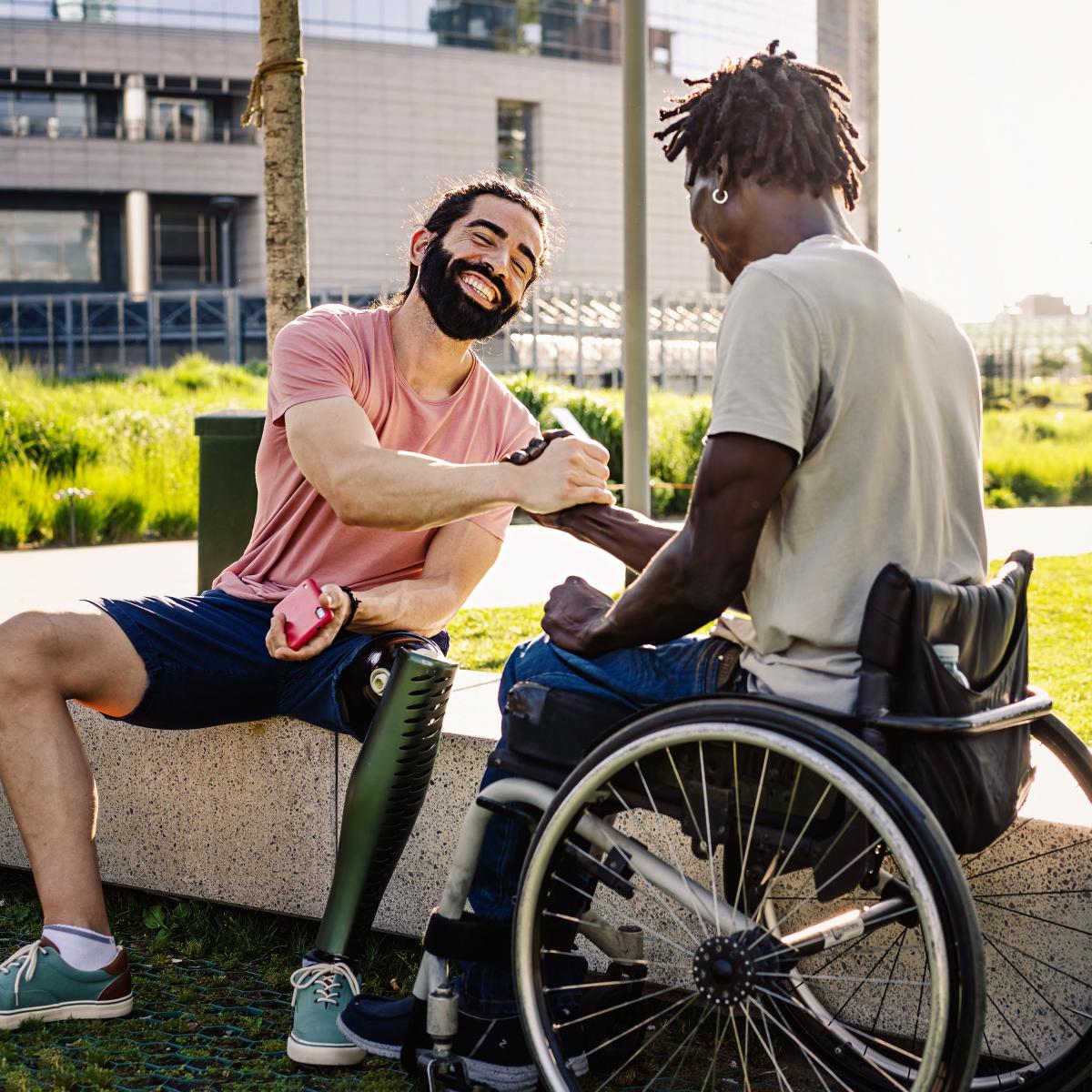 Two young adults who are living with disabilities share a laugh and a handshake outside